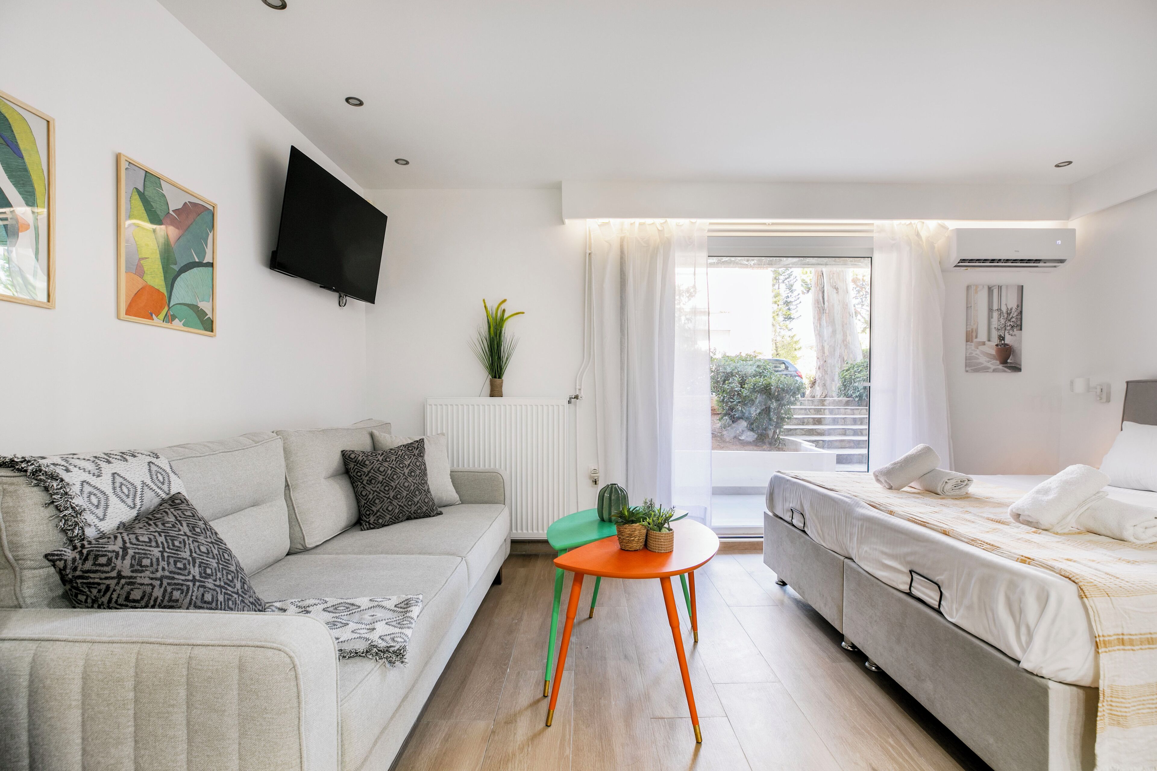 Una sala moderna con sofá, una mesita, una cama y un televisor montado en la pared.