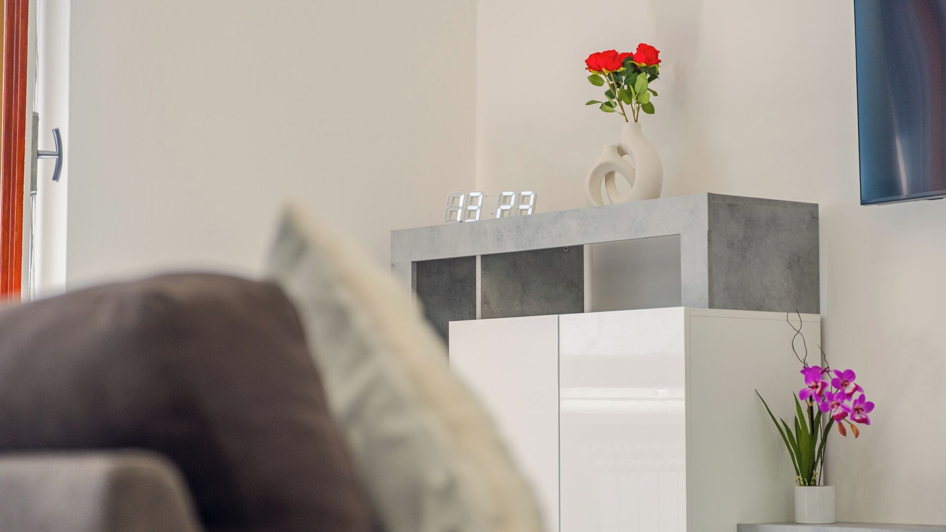 Una sala de estar moderna con un sofá, un armario blanco con un reloj y dos jarrones con flores.