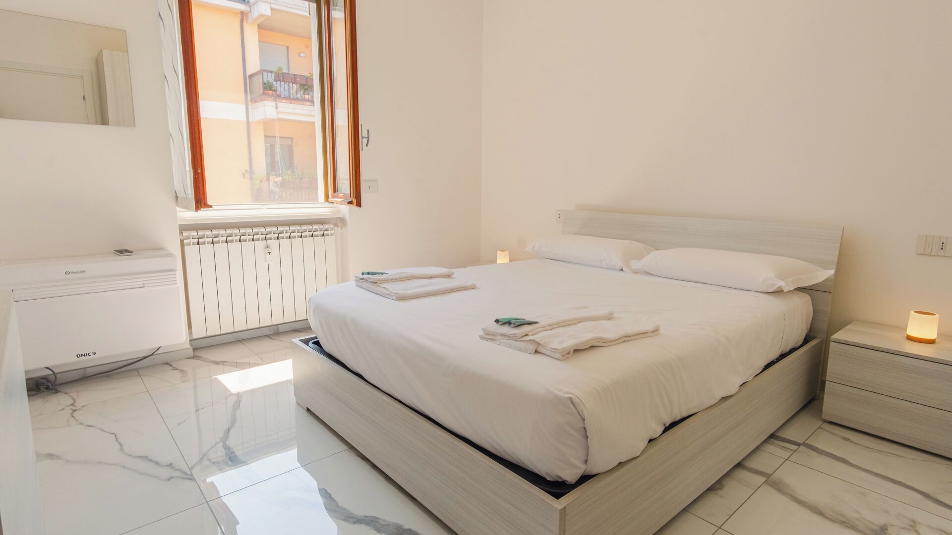 Une chambre d’hôtel avec un lit, des tables de chevet, un radiateur, une fenêtre et un miroir.
