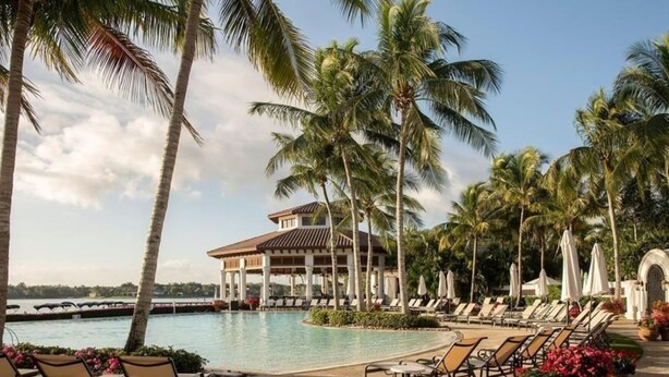 A resort pool area with lounge chairs and a building with a tiled roof. - Luxury Waterfront Rental with wraparound water views at Miromar Lakes, (Miromar Lakes)