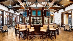 A spacious bar area with high ceilings and exposed beams, featuring multiple bar stools and a central bar counter. - Luxury Waterfront Rental with wraparound water views at Miromar Lakes, (Miromar Lakes)
