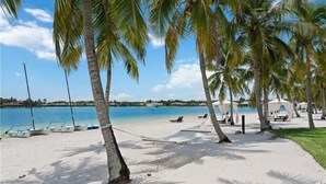 A beach with palm trees, a hammock, and boats on the water. - Luxury Waterfront Rental with wraparound water views at Miromar Lakes, (Miromar Lakes)