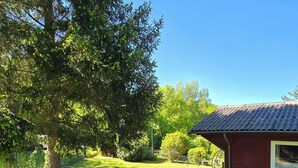 A red house with a tiled roof, surrounded by a grassy yard and a large tree. - Cozy TinyHouse with garden in the nature park (Rorodt)