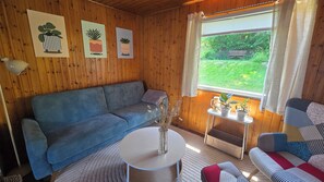 A cozy room with a blue sofa, a small white table, and a window with a view of greenery. - Cozy TinyHouse with garden in the nature park (Rorodt)