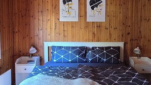 A wooden-paneled bedroom with a bed, two bedside tables, and a ceiling light fixture. - Cozy TinyHouse with garden in the nature park (Rorodt)