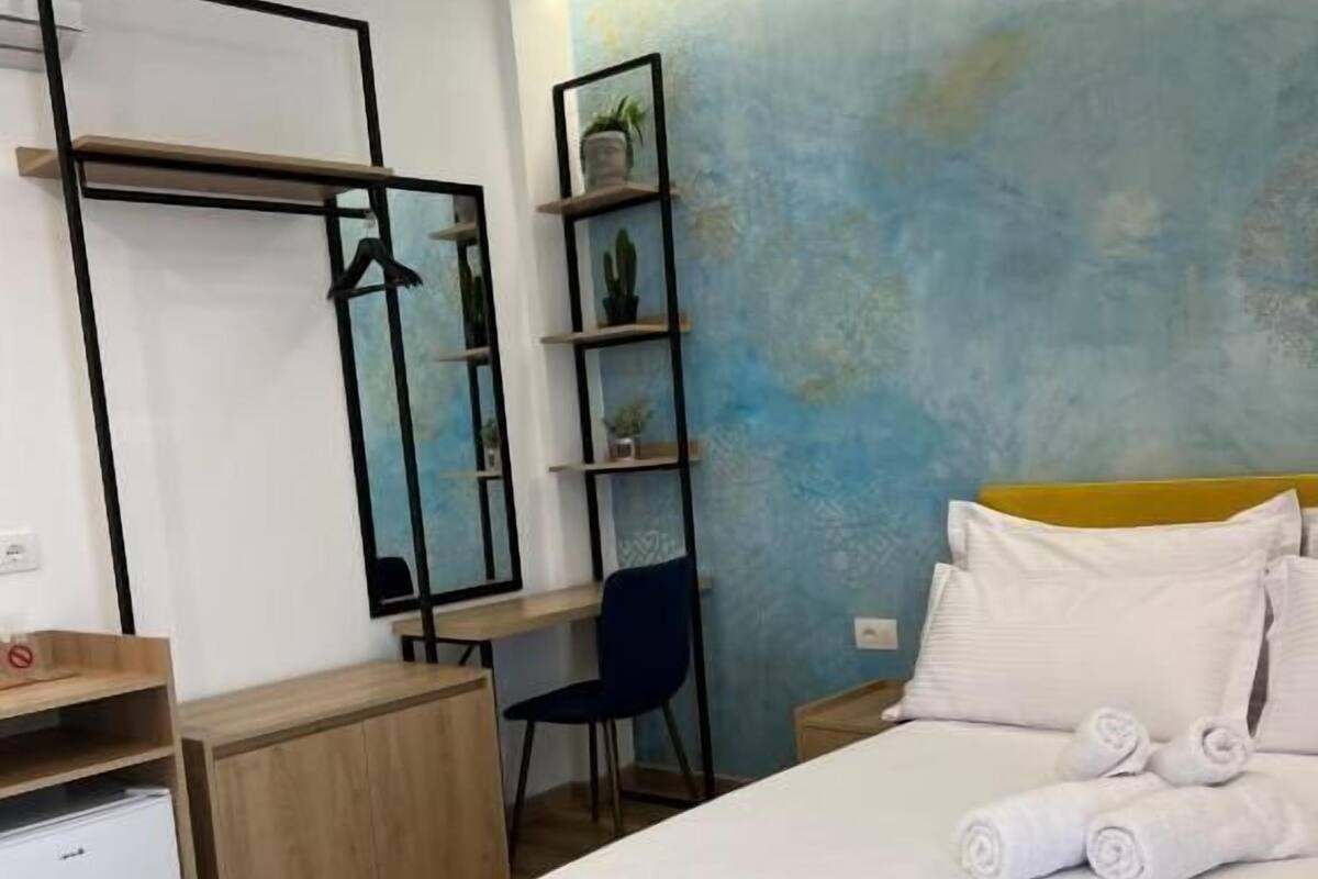 A modern hotel room with a bed, a desk, a chair, and a small refrigerator.