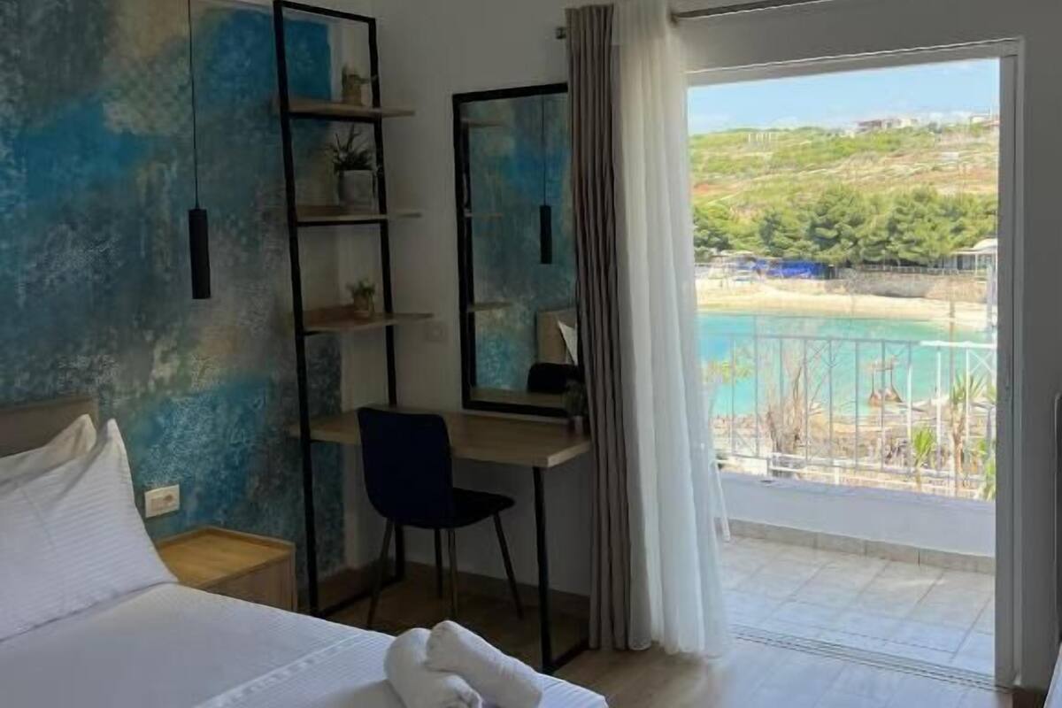 A hotel room with a bed, a desk, a chair, and a view of a pool and greenery.