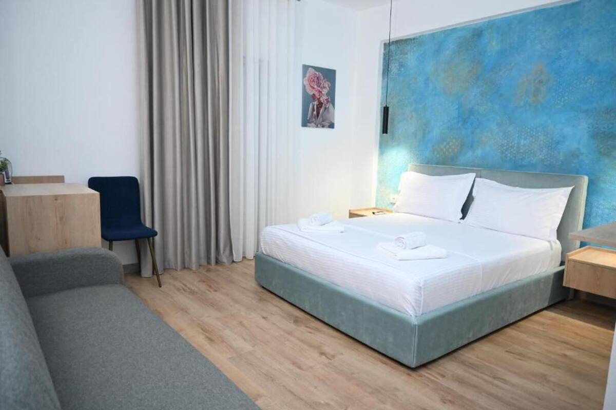 A modern hotel room with a large bed, a desk, a chair, and a blue accent wall.