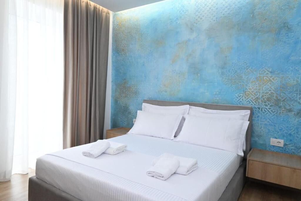 A neatly made bed with white linens and towels, a wooden headboard, and a blue patterned wall.