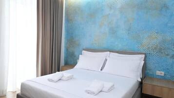 A neatly made bed with white linens and towels, a wooden headboard, and a blue patterned wall.