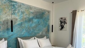 A hotel room with two beds, a large abstract painting on the wall, a framed artwork, and a window with curtains. - EMAR Beachfront Hotel Ksamil (Ksamil)
