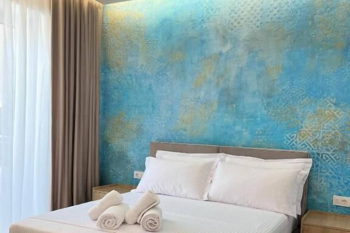 A hotel room with a large bed, white linens, and a blue patterned wall.