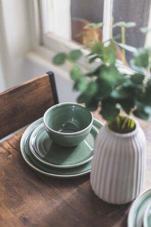 A wooden table with a green bowl and matching plates, a white ribbed vase, and a potted plant. - Chic Kensington Apt w/Garden! Sleeps 5 & only 4  Min Walk To Station! (London)