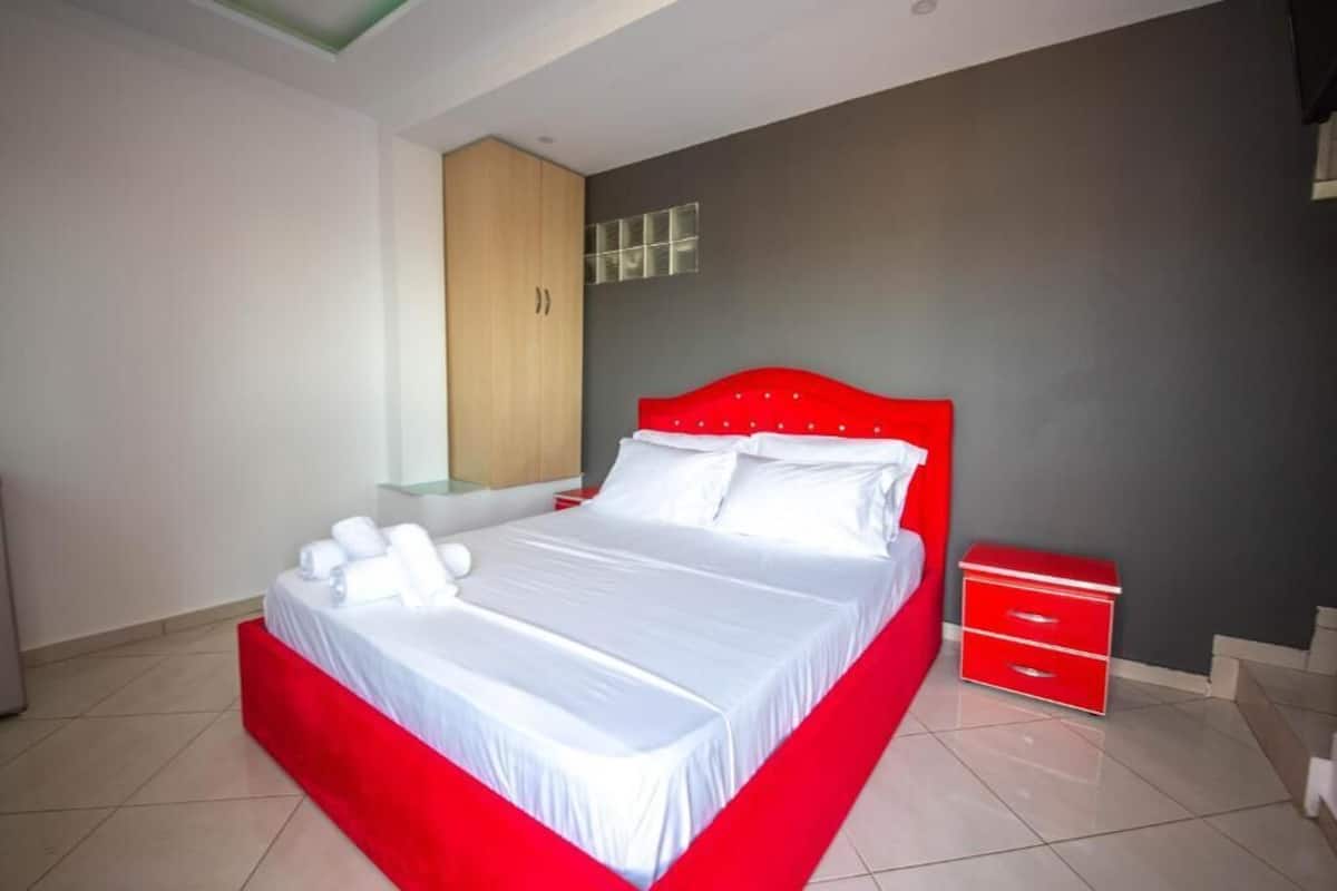 Une chambre à coucher moderne avec un cadre de lit rouge, une literie blanche et une table de chevet rouge dotée de tiroirs.