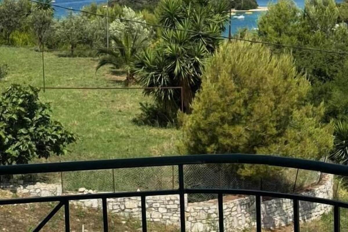 Une vue sur la côte, avec un ciel dégagé, une zone herbeuse parsemée d’arbres, et une vue lointaine sur la mer et une petite île.