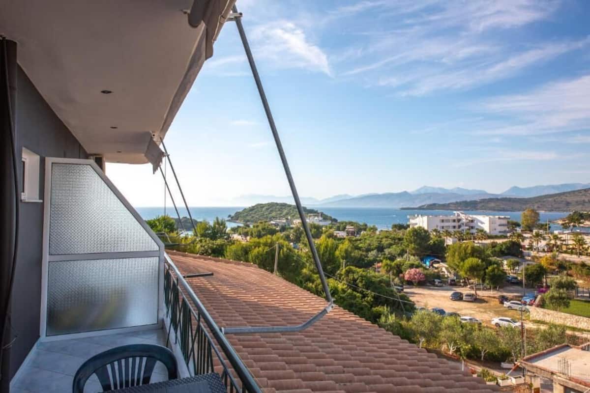 Un balcon donnant sur une ville côtière, avec un toit recouvert de tuiles et une balustrade.