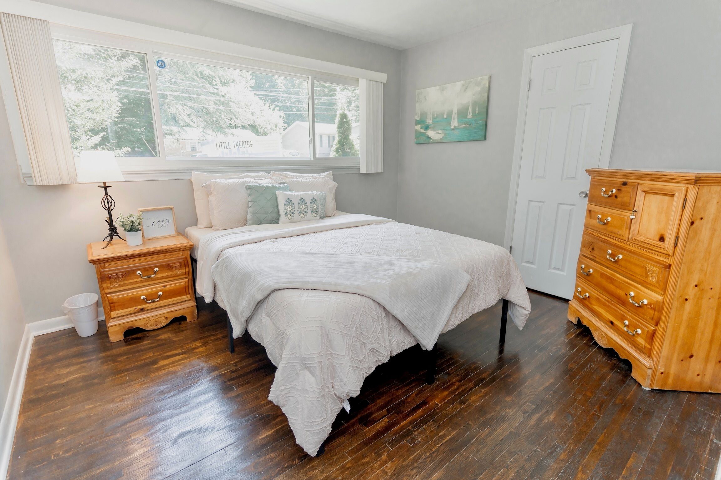 Un dormitorio con una cama grande, cómoda de madera y ventana con vistas a árboles.