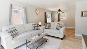A modern living room with two sofas, a coffee table, a clock, and a ceiling fan. - Cozy Pet Friendly 3BR - Fenced Yard - 1Mi HPU & DwnTwn - Furniture Market (High Point)