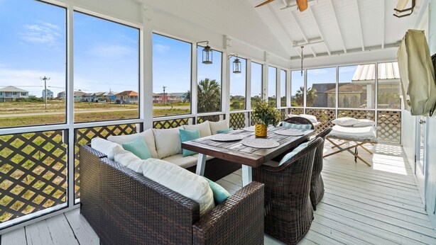 A covered outdoor area with wicker furniture, a table, and a ceiling fan.