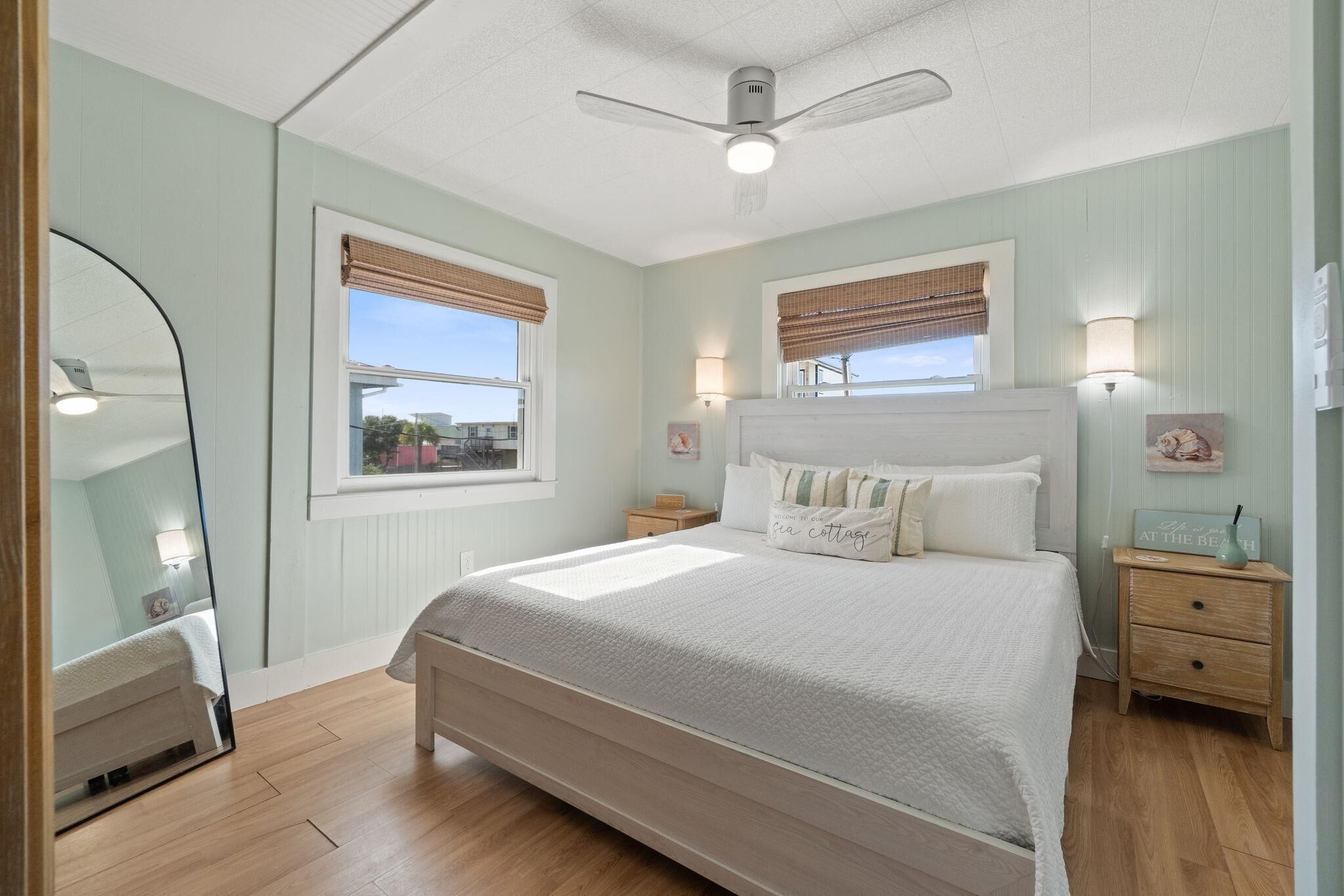 Une chambre à coucher comprenant un lit, des tables de chevet, un ventilateur de plafond et des fenêtres équipées de stores.