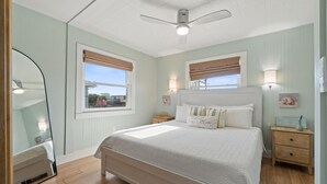 A bedroom with a bed, bedside tables, a ceiling fan, and windows with blinds.