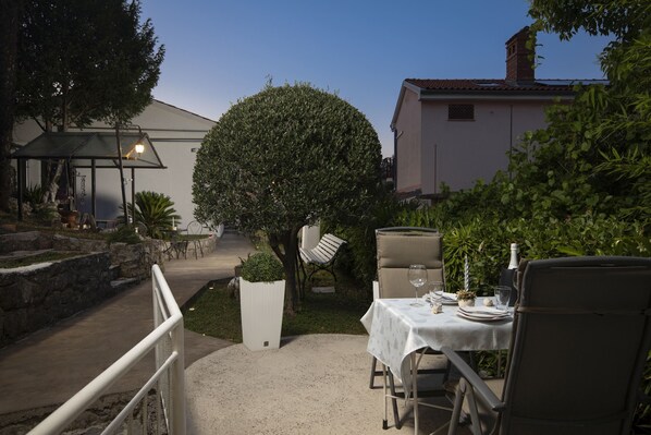 An outdoor dining area with a table set for two, surrounded by greenery and a stone wall.