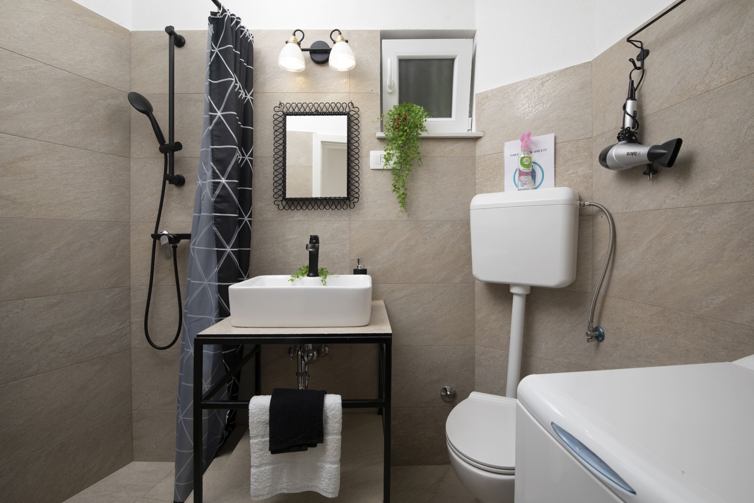 A modern bathroom with a shower, toilet, sink, and a hairdryer mounted on the wall.