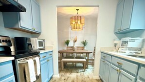 A modern kitchen with light blue cabinets, a stainless steel oven, a microwave, and a dining area with a wooden table and chairs. - Completely renovated luxury home. Putt putt golf, bocce, etc.  Walk to downtown! (St. Augustine)