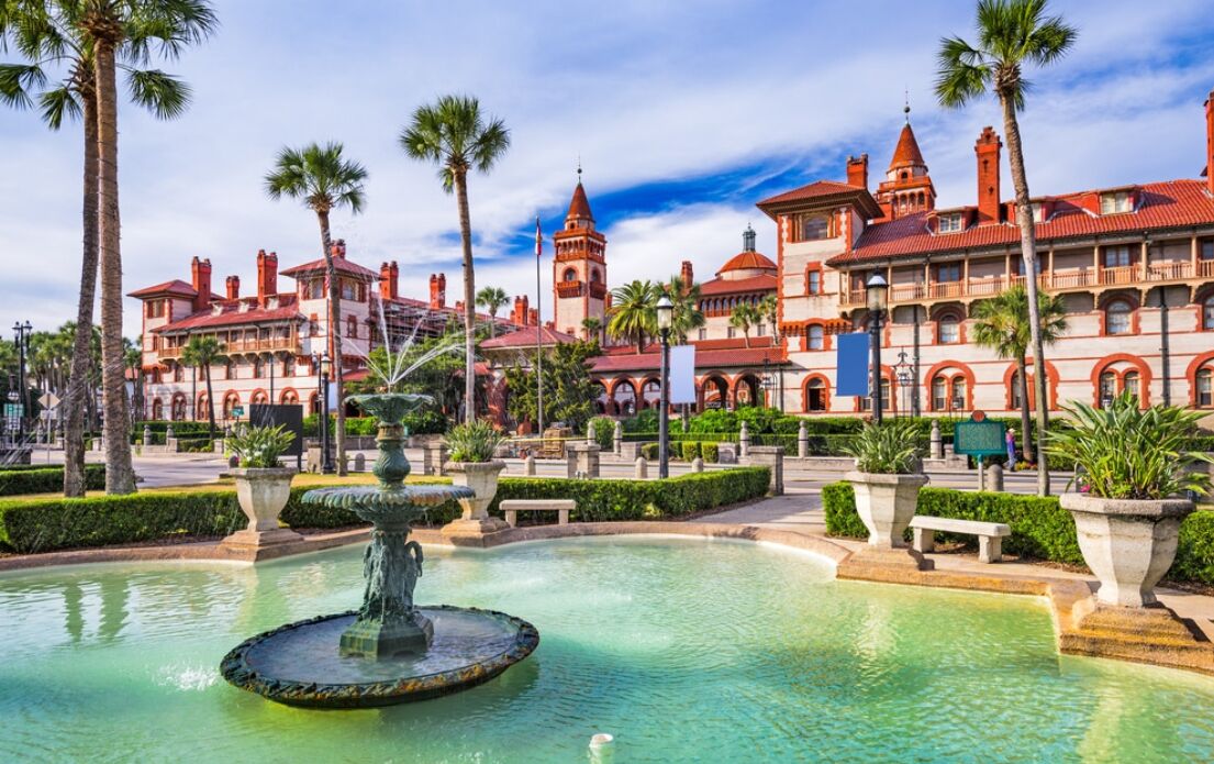 A historic building with a fountain, palm trees, and a clear sky.