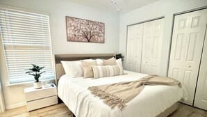 A bedroom with a bed, a ceiling fan, a window with blinds, a bedside table with a plant, and a door. - Completely renovated luxury home. Putt putt golf, bocce, etc.  Walk to downtown! (St. Augustine)