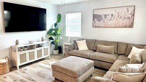 A living room with a large flat-screen TV, a ceiling fan, a large plant, a beige sofa, and a framed picture on the wall. - Completely renovated luxury home. Putt putt golf, bocce, etc.  Walk to downtown! (St. Augustine)