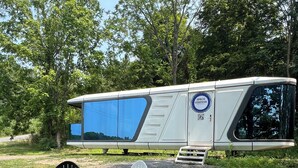 En husbil för camping, med en eldstad och två Adirondack-stolar placerade på en grusplan.