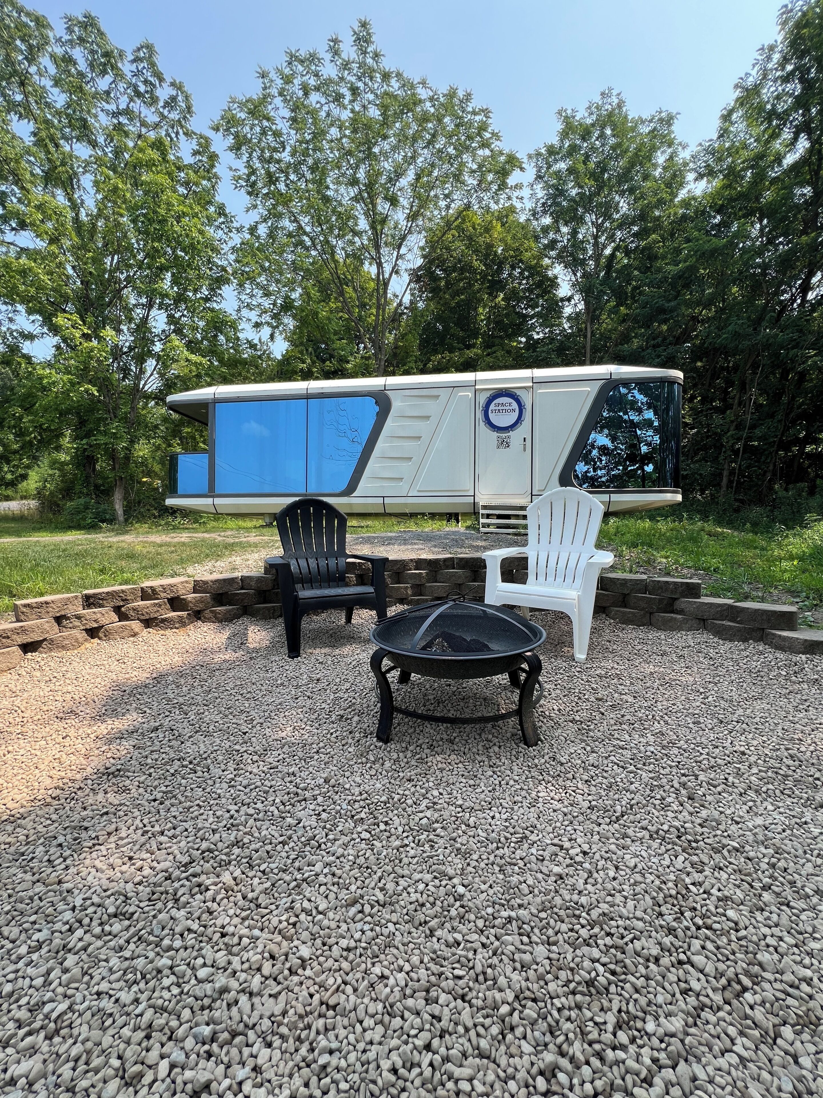 A space-themed RV with a blue exterior, two chairs, and a fire pit in a gravel area.