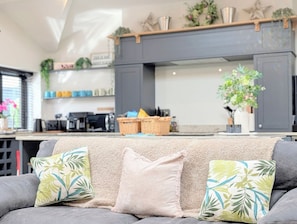 Una sala de estar moderna con un sofá gris, una chimenea y una cocina al fondo.