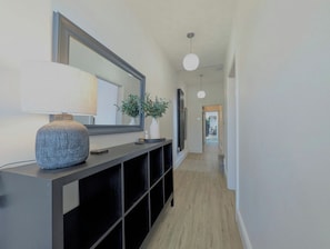 A hallway with a dark console table, a large mirror, a hanging light fixture, and a plant.