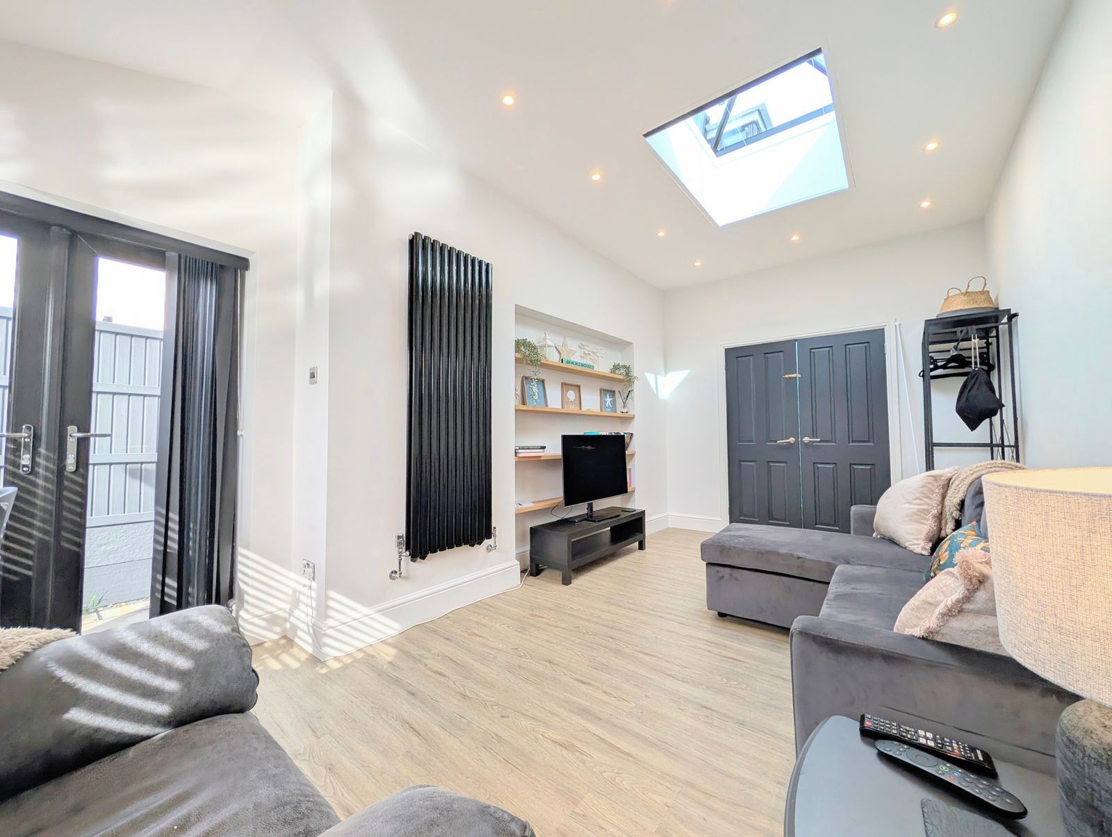 A modern living room with a flat-screen TV, grey sofas, a ceiling light, and a door.