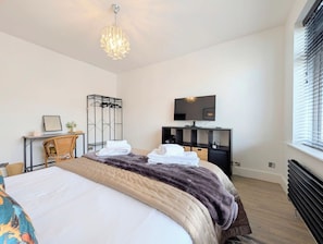 A hotel room with a bed, a television, a desk with a chair, a mirror, and a radiator.