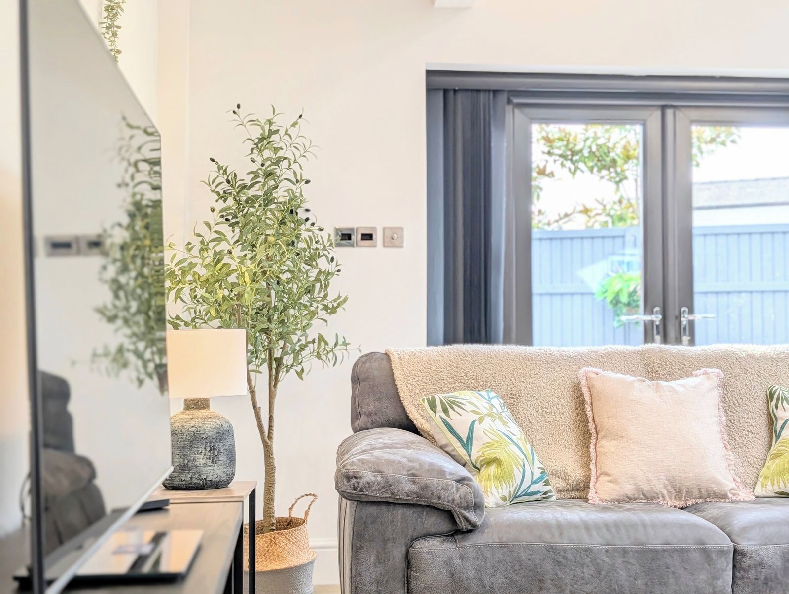 Een moderne woonkamer met een grijze bank, een lamp en een potplant.