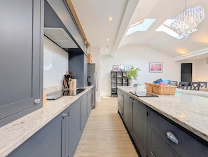 A modern kitchen with dark cabinetry, a marble countertop, and a central island. - Birkdale Links Lodge (Southport)