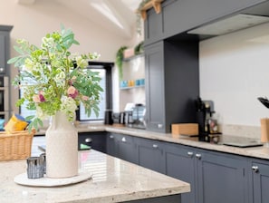 A kitchen with a white vase containing flowers on a marble countertop.