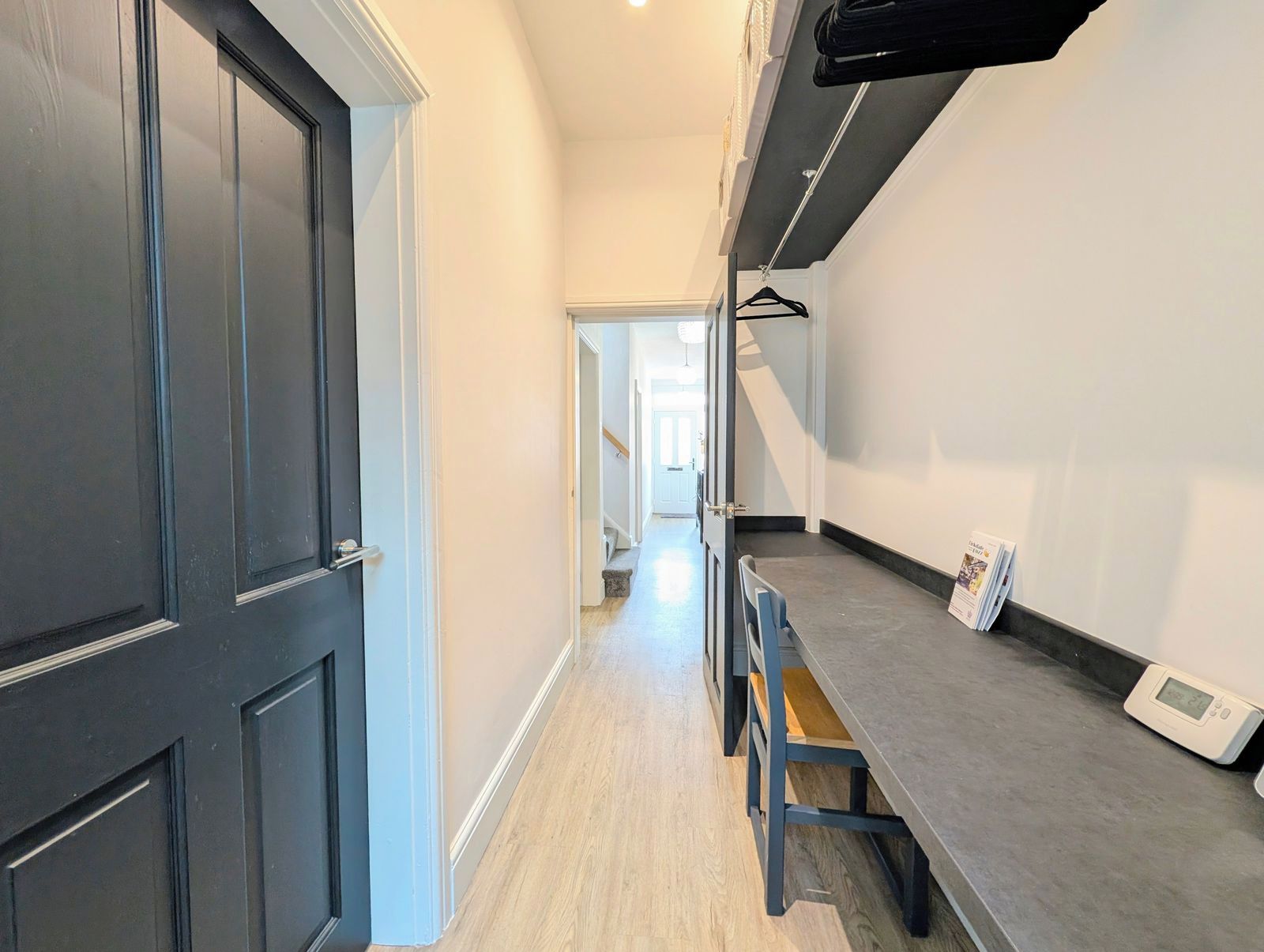 A hallway with a dark door, a light-colored wall, and a grey countertop with a digital thermostat.