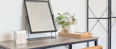 Un escritorio con una taza blanca, un espejo en marco, una cesta de mimbre y una planta pequeña sobre una mesa de madera.
