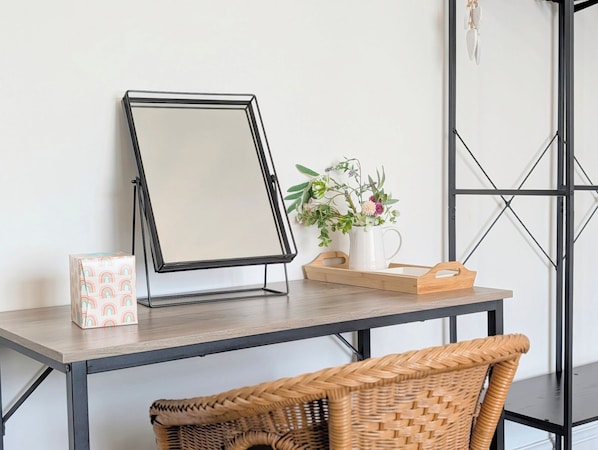 A desk with a white mug, a framed mirror, a wicker basket, and a small plant on a wooden table.