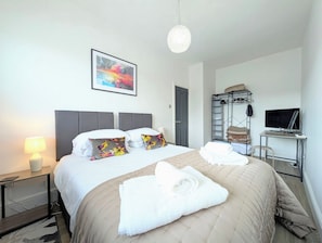 Une chambre d’hôtel avec un lit, un bureau, une télévision, une armoire et un tableau au mur.