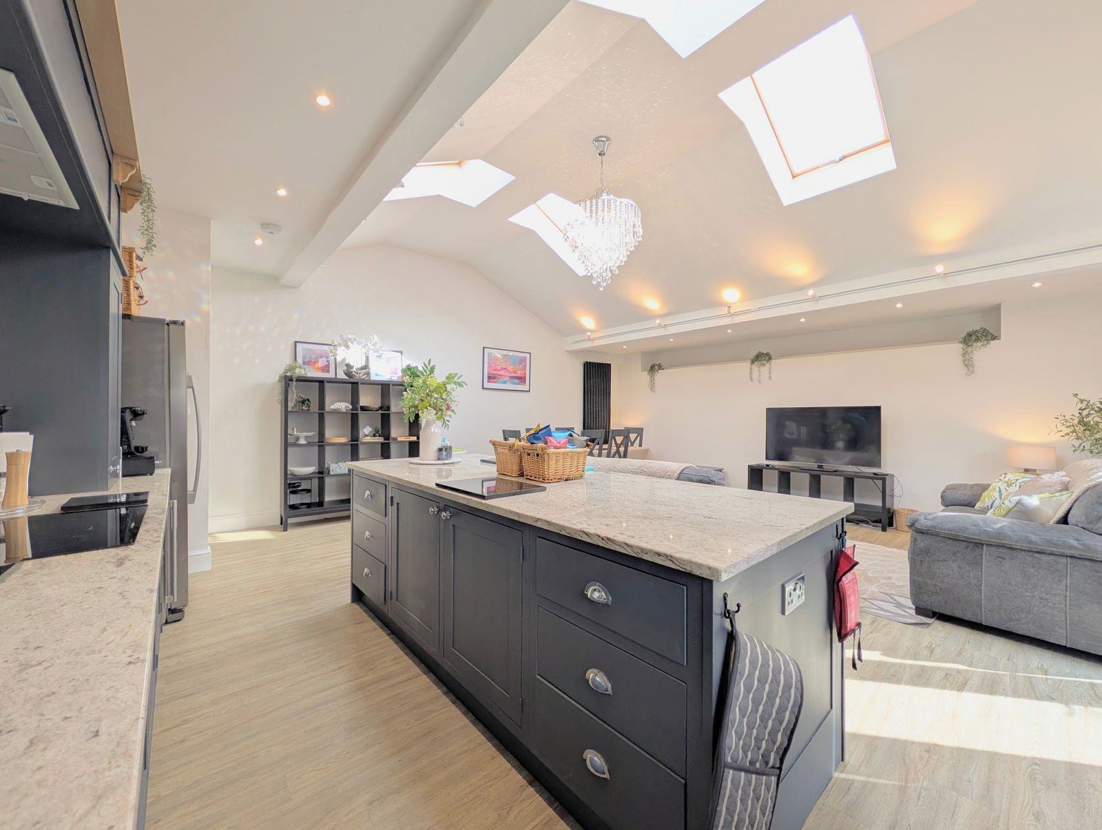 A modern kitchen with dark cabinetry, a central island, and a dining area with a grey sofa.