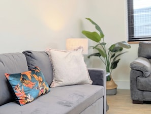 A grey sofa with floral and solid pillows, a potted plant, and a grey armchair in a living room.