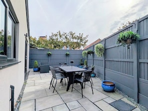 Un espace patio avec une table et des chaises, une clôture grise et des plantes en pot.