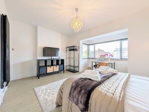 A bedroom with a bed, a TV on a stand, a wardrobe, a window with a view, and a chandelier.