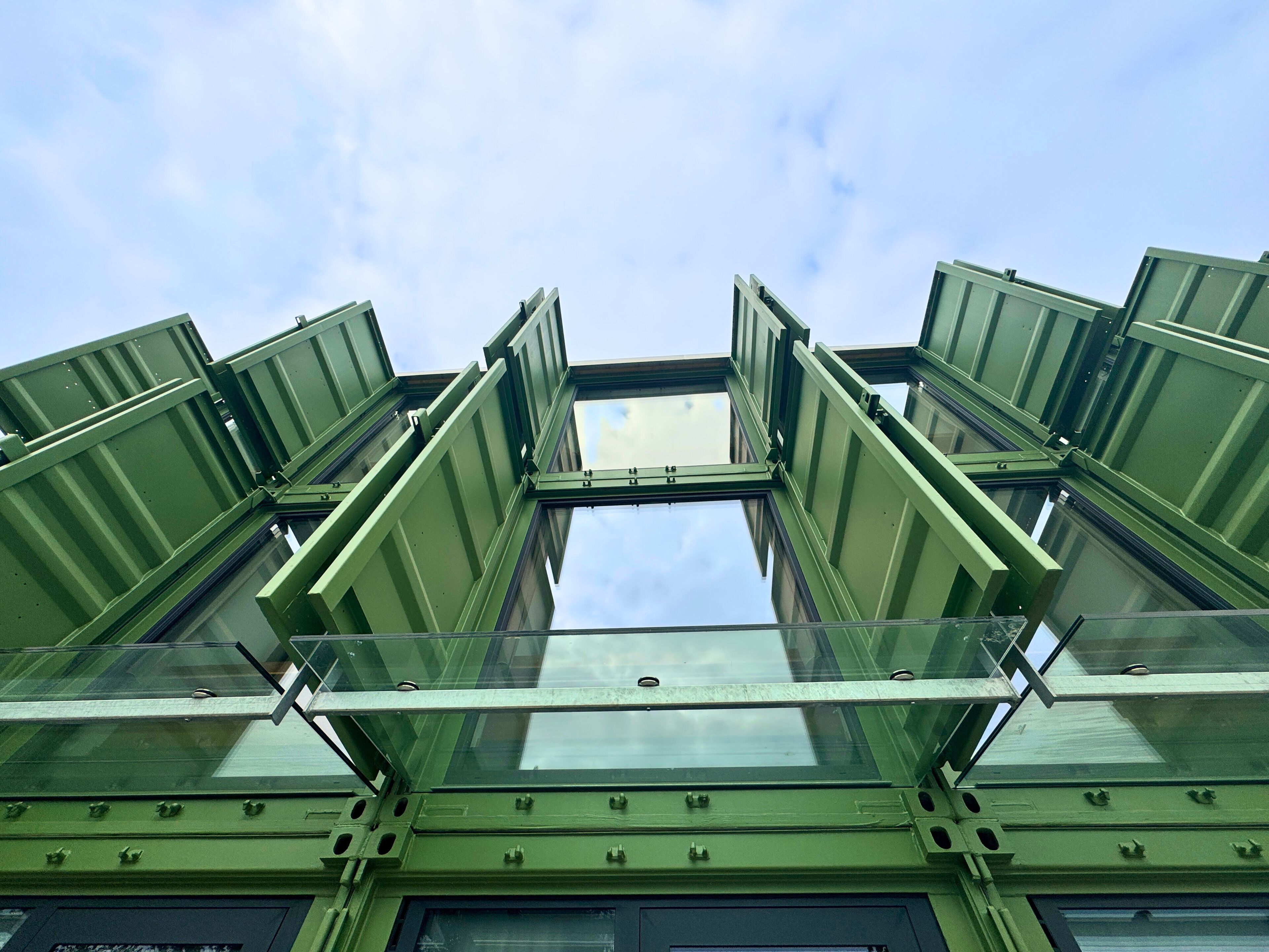 A modern building with a unique architectural design featuring large, green, angled metal frames and glass panels.