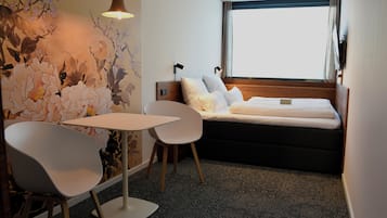 Quarto de hotel com cama, mesa, duas cadeiras, um mural na parede e uma janela com cortinas.